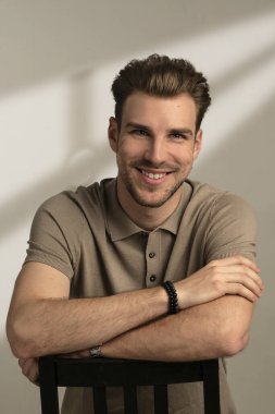 Tecrit edilmiş arka planda oturan yakışıklı bir gencin stüdyo fotoğrafı. Polo tişört giyen ve kameraya gülümseyen kendinden emin bir erkek. Uzayı kopyala İzole edilmiş arkaplan. 