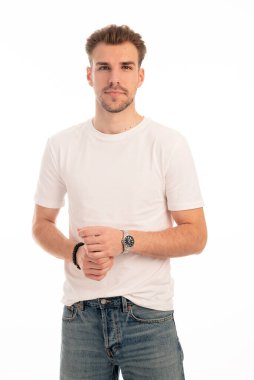 İzole edilmiş arka planda duran genç bir adamın stüdyo çekimi. Beyaz tişört giyen ve kameraya bakan kendinden emin bir erkek. Boşluğu kopyala.