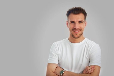 İzole edilmiş arka planda duran genç bir adamın stüdyo çekimi. Beyaz tişört giyen ve kameraya bakan kendinden emin bir erkek. Boşluğu kopyala.