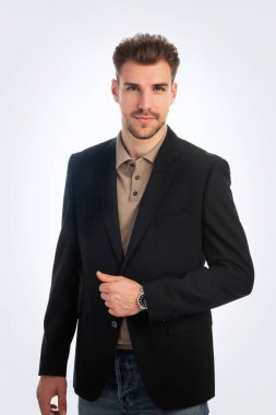 Beyaz arka planda duran yakışıklı bir iş adamının stüdyo fotoğrafı. Polo tişört ve spor ceket giyen kendinden emin bir erkek. Uzayı kopyala İzole edilmiş arkaplan.