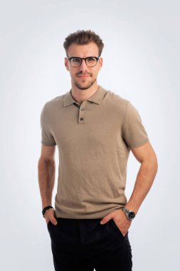 Beyaz arka planda oturan yakışıklı bir gencin stüdyo fotoğrafı. Polo tişört giyen ve kameraya gülümseyen kendinden emin bir erkek. Uzayı kopyala İzole edilmiş arkaplan. 
