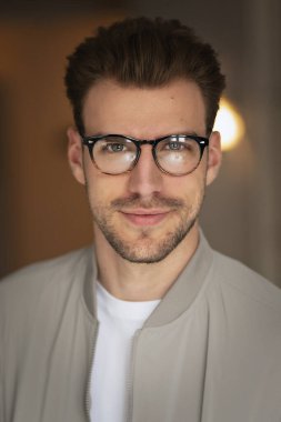 Kameraya bakıp gülümseyen genç bir adamın vesikalığı. Beyaz gömlek ve ceket giyen ve içeride duran kendine güvenen bir adam.. 