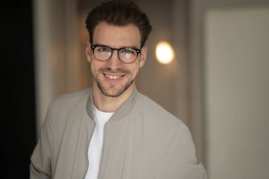 Kameraya bakıp gülümseyen genç bir adamın vesikalığı. Beyaz gömlek ve ceket giyen ve içeride duran kendine güvenen bir adam.. 