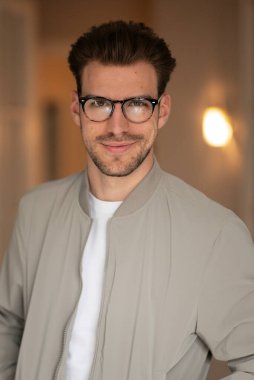 Kameraya bakıp gülümseyen genç bir adamın vesikalığı. Beyaz gömlek ve ceket giyen ve içeride duran kendine güvenen bir adam.. 