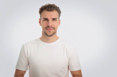 İzole edilmiş arka planda duran genç bir adamın stüdyo çekimi. Beyaz tişört giyen ve kameraya bakan güvenilir bir erkek. Boşluğu kopyala.