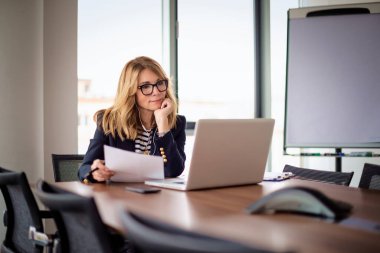 Sarı saçlı iş kadını dizüstü bilgisayar kullanıyor ve iş yerinde internet konferansı yapıyor. Olgun bir bayan patronun portresi, müdür ve CEO internette geziniyor ve online planlama yapıyor. İş kıyafeti giyen çekici bir kadın.. 