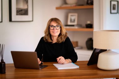 Evde dizüstü bilgisayarının önünde oturan ve video konferansı yapan sarışın bir kadın. Evden çalışan orta yaşlı beyaz bir kadın. Merkez Ofis. 