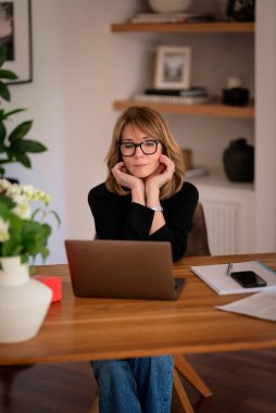 Evde dizüstü bilgisayarının önünde oturan ve video konferansı yapan sarışın bir kadın. Evden çalışan orta yaşlı beyaz bir kadın. Merkez Ofis. 