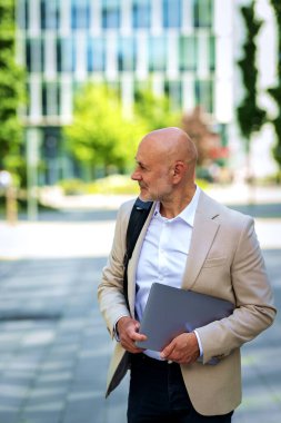 Diz üstü bilgisayarı ve sırt çantası olan orta yaşlı bir adam şehir caddesinde yürüyor. Kendine güveni tam bir iş adamı.. 