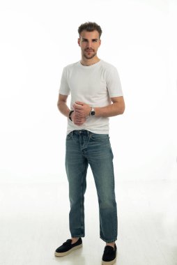 İzole edilmiş arka planda duran genç bir adamın stüdyo çekimi. Beyaz tişört ve kot pantolon giyen kendinden emin bir erkek. Uzayı kopyala Tam boy çekim. 