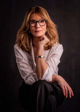 Esmer arka planda orta yaşlı bir kadının stüdyo portresi. İzole edilmiş arka planda oturan sarı saçlı kadın. Boşluğu kopyala. 