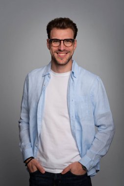 Tecrit edilmiş arka planda duran yakışıklı bir gencin stüdyo fotoğrafı. Tişört giyen ve kameraya bakan kendinden emin bir erkek. Uzayı kopyala İzole edilmiş arka plan. Eller çenede.. 