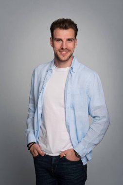 Tecrit edilmiş arka planda duran yakışıklı bir gencin stüdyo fotoğrafı. Tişört giyen ve kameraya bakan kendinden emin bir erkek. Uzayı kopyala İzole edilmiş arka plan. Eller çenede.. 