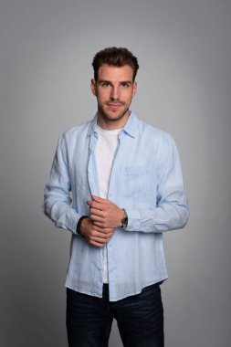 Tecrit edilmiş arka planda duran yakışıklı bir gencin stüdyo fotoğrafı. Tişört giyen ve kameraya bakan kendinden emin bir erkek. Uzayı kopyala İzole edilmiş arka plan. Eller çenede.. 