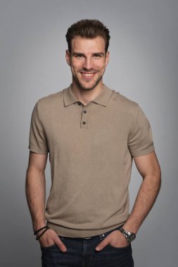 Tecrit edilmiş arka planda duran yakışıklı bir gencin stüdyo fotoğrafı. Polo tişört giyen ve kameraya bakan kendinden emin bir erkek. Uzayı kopyala İzole edilmiş arkaplan. 