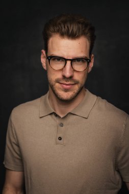 Tecrit edilmiş arka planda duran yakışıklı bir gencin stüdyo fotoğrafı. Polo tişört giyen ve kameraya bakan kendinden emin bir erkek. Uzayı kopyala İzole edilmiş koyu arkaplan.