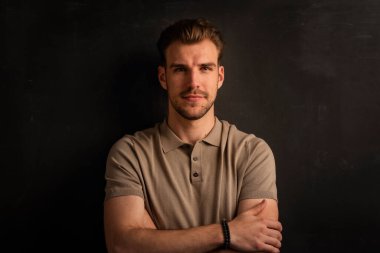 Tecrit edilmiş arka planda duran yakışıklı bir gencin stüdyo fotoğrafı. Polo tişört giyen ve kameraya bakan kendinden emin bir erkek. Uzayı kopyala İzole edilmiş koyu arkaplan.