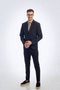 İzole edilmiş beyaz arka plana karşı duran yakışıklı bir gencin stüdyo fotoğrafı. Kendine güvenen erkek takım elbiseli ve kameraya bakıyor. Uzayı kopyala İzole edilmiş arka plan. Tam uzunluk. 