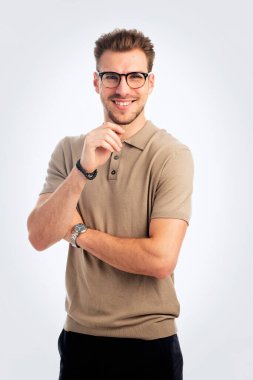 Tecrit edilmiş arka planda duran yakışıklı bir gencin stüdyo fotoğrafı. Polo tişört giyen ve kameraya bakan kendinden emin bir erkek. Uzayı kopyala İzole edilmiş arka plan. Eller çenede.. 