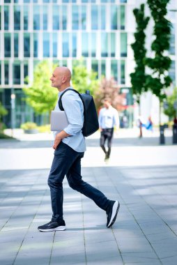Şehirde iş bölgesinde yürüyen yakışıklı bir adam. Orta yaşlı iş adamı iş kıyafeti giyiyor ve elinde bilgisayar laptopu tutuyor.. 