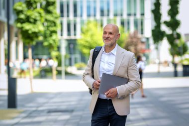 Şehirde iş bölgesinde yürüyen yakışıklı bir adam. Orta yaşlı iş adamı iş kıyafeti giyiyor ve elinde bilgisayar laptopu tutuyor.. 