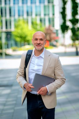 Şehirde iş bölgesinde yürüyen yakışıklı bir adam. Orta yaşlı iş adamı iş kıyafeti giyiyor ve elinde bilgisayar laptopu tutuyor.. 