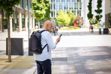 Şehirde iş bölgesinde yürüyen yakışıklı bir adam. Orta yaşlı iş adamı sırt çantası takıyor ve akıllı telefonunu kullanıyor.. 