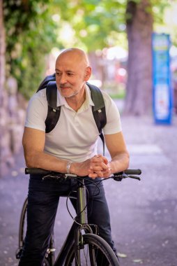 Sokakta bisiklet kullanan orta yaşlı bir adam. Banliyö çalışanı işe gidiyor ve günlük kıyafetler giyiyor.. 