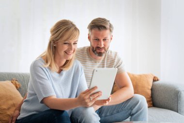 Orta yaşlı bir çift evdeki kanepede dokunmatik ped kullanıyor. Sarı saçlı kadın ve ağda gezinen gri saçlı adam.. 