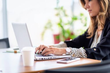 Kendine güveni tam bir iş kadını masasında oturuyor ve bilgisayarını kullanıyor. Modern bir ofiste çalışan profesyonel bir kadın..