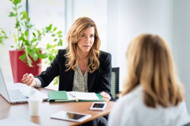 Bir grup iş kadını masa başında oturup iş görüşmesi yaparken dizüstü bilgisayar kullanıyor. Modern bir ofiste takım çalışması..