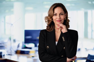 Ofiste duran kendine güvenen bir iş kadını. Profesyonel kadın iş kıyafeti giyiyor ve kameraya bakıyor.. 