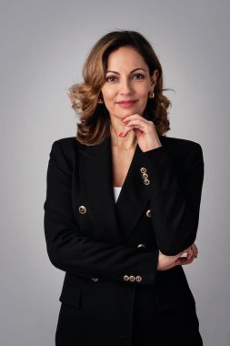 Tecrit edilmiş arka planda duran kendinden emin orta yaşlı bir kadının stüdyo portresi. İş kıyafeti giyen kendine güvenen bir kadın. Boşluğu kopyala. 