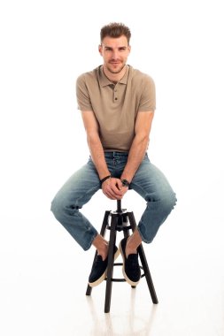 İzole edilmiş beyaz arka planda oturan yakışıklı bir gencin stüdyo fotoğrafı. Kendine güvenen erkek iş kıyafeti giyiyor ve kameraya bakıyor. Uzayı kopyala İzole edilmiş arkaplan.