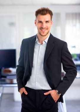 Görevde duran başarılı genç iş adamının portresi. Profesyonel iş adamı kameraya bakıyor ve gülümsüyor..