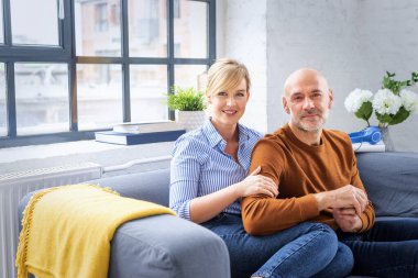 Sarı saçlı bir kadın ve koltukta oturan orta yaşlı bir adam. Orta yaşlı bir çift gündelik giysiler giyiyor ve birlikte vakit geçiriyorlar..