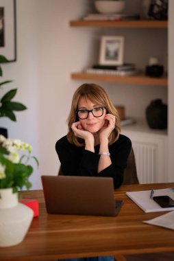 Evde dizüstü bilgisayarının önünde oturan ve video konferansı yapan sarışın bir kadın. Evden çalışan orta yaşlı beyaz bir kadın. Merkez Ofis. 