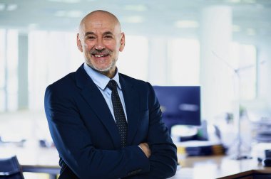 İdari işadamı ofiste duruyor. Kendine güvenen erkek takım elbiseli ve kameraya gülümsüyor. Yakın çekim.. 