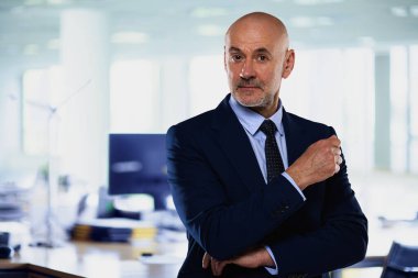 İdari işadamı ofiste duruyor. Kendine güvenen erkek takım elbiseli ve kameraya gülümsüyor. Yakın çekim.. 