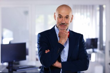 İdari işadamı ofiste duruyor. Kendine güvenen erkek takım elbiseli ve kameraya gülümsüyor.. 