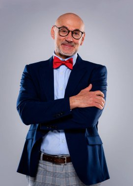 Tecrit edilmiş arka planda duran yaşlı adamın stüdyo portresi. Uzayı kopyala Takım elbiseli, kırmızı papyonlu ve kameraya gülümseyen kendinden emin bir erkek..