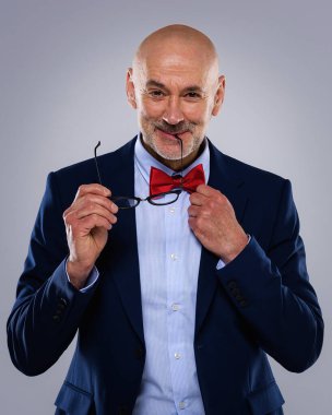 Tecrit edilmiş arka planda duran yaşlı adamın stüdyo portresi. Uzayı kopyala Takım elbiseli, kırmızı papyonlu ve kameraya gülümseyen kendinden emin bir erkek..