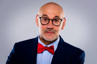 Tecrit edilmiş arka planda duran son sınıf öğrencisinin yakın çekimi. Uzayı kopyala Takım elbiseli, kırmızı papyonlu ve kameraya gülümseyen kendinden emin bir erkek..