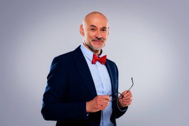 Tecrit edilmiş arka planda duran yaşlı adamın stüdyo portresi. Uzayı kopyala Takım elbiseli, kırmızı papyonlu ve kameraya gülümseyen kendinden emin bir erkek..