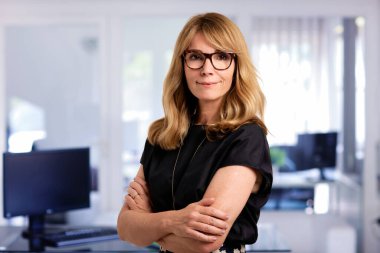 Ofiste kendine güvenen ve kameraya bakan bir iş kadını. Orta yaşlı profesyonel kadın iş kıyafeti giyiyor ve gülümsüyor. Boşluğu kopyala. 