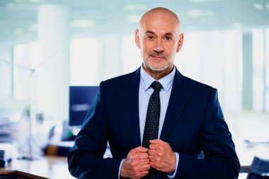 İdari işadamı ofiste duruyor. Kendine güvenen erkek takım elbiseli ve kameraya gülümsüyor. Yakın çekim.. 