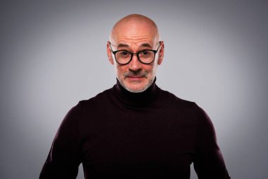 Tecrit edilmiş arka planda duran yaşlı bir adamın stüdyo çekimi. Kendine güvenen erkek balıkçı yaka kazak giyiyor ve hayret içinde kameraya bakıyor. Uzayı kopyala Belini kaldır.. 