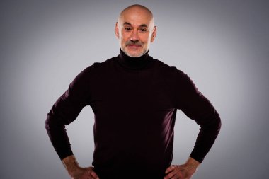 Tecrit edilmiş arka planda duran yaşlı bir adamın stüdyo çekimi. Kendine güvenen erkek balıkçı yaka kazak giyiyor ve kameraya bakıyor. Uzayı kopyala Belini kaldır.. 