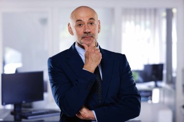 İdari işadamı ofiste duruyor. Kendine güvenen erkek takım elbiseli ve kameraya gülümsüyor.. 