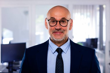 İdari işadamı ofiste duruyor. Kendine güvenen erkek takım elbiseli ve kameraya gülümsüyor. Yakın çekim.. 